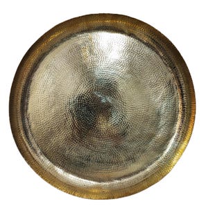 May include: A round, hammered metal tray with a gold-colored rim and a silver-colored center. The tray has a textured surface with a dimpled pattern. The rim is a darker gold than the center, creating a contrast.
