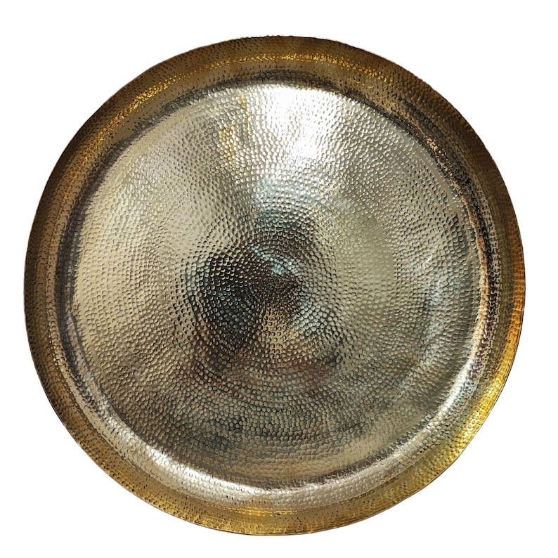 May include: A round, hammered metal tray with a gold-colored rim and a silver-colored center. The tray has a textured surface with a dimpled pattern. The rim is a darker gold than the center, creating a contrast.