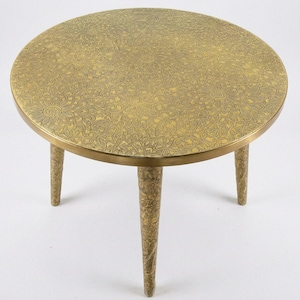 Peut inclure: Une table d'appoint ronde de couleur laiton avec trois pieds. Le plateau présente un motif floral complexe. La table mesure environ 50 cm de diamètre et 46 cm de haut.