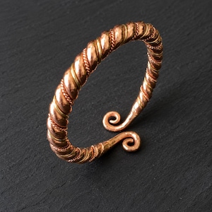 May include: A copper-colored metal cuff bracelet featuring a twisted, rope-like texture throughout the band. The bracelet has an open design with two ends that terminate in small, outward-facing spiral curls, creating a continuous metallic loop.