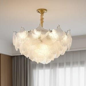 Könnte beinhalten: Eine moderne Deckenleuchte mit goldfarbener Deckenhalterung und einem strukturierten, mattierten Glasschirm. Der Schirm ist in Form überlappender Blätter gestaltet und erzeugt ein weiches, diffuses Licht. Sie hängt an einem beigen Kabel.