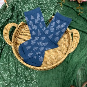May include: Navy blue socks with a white tree design, presented in a woven basket. The socks are folded and rest on a green fabric. The socks are made of a soft material. The basket has a handle.