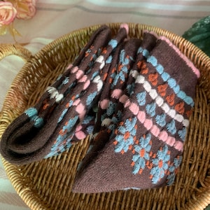 May include: A pair of brown socks with a floral pattern in light blue, pink, white, and orange. The socks are folded and placed in a woven basket. The socks have a pink trim.