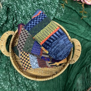 May include: A woven basket holds several pairs of patterned socks. The socks feature various geometric designs in shades of blue, green, yellow, orange, and brown. The basket sits on a green fabric background.
