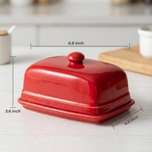 Op de afbeelding: Een glanzend rode keramische boterdoos met een deksel en een kleine knop. De doos is 17,3 cm lang, 11,4 cm breed en 9,1 cm hoog. De boterdoos is ontworpen om een standaard blok boter in te bewaren.