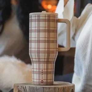 Może przedstawiać: Kremowy, izolowany kubek z czerwono-brązowym wzorem w kratę. Kubek ma pasującą pokrywkę i duży uchwyt. Słowa "HYDRO JUG" są wydrukowane pionowo z boku.