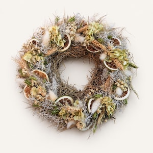 Peut inclure: Une couronne circulaire faite de brindilles et d'herbes brunes séchées, ornée de fleurons d'hortensia verts séchés, d'herbe à queue de lapin blanche, de tiges de blé et de plusieurs fines tranches circulaires d'agrumes séchés disposées.