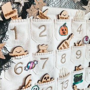 Peut inclure: Un calendrier de l'avent en feutre blanc avec 24 poches, chacune avec un num&eacute;ro brod&eacute; en or. Les poches contiennent diverses d&eacute;corations sur le th&egrave;me d'Halloween, notamment des fant&ocirc;mes, des citrouilles, des bonbons et un chaudron de sorci&egrave;re. Le calendrier est d&eacute;cor&eacute; d'&eacute;toiles dor&eacute;es paillet&eacute;es.