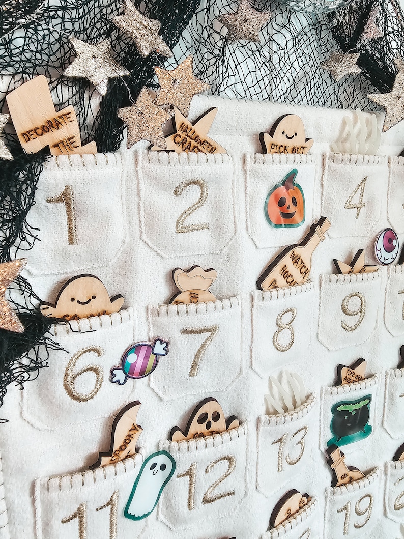 Peut inclure: Un calendrier de l'avent en feutre blanc avec 24 poches, chacune avec un num&eacute;ro brod&eacute; en or. Les poches contiennent diverses d&eacute;corations sur le th&egrave;me d'Halloween, notamment des fant&ocirc;mes, des citrouilles, des bonbons et un chaudron de sorci&egrave;re. Le calendrier est d&eacute;cor&eacute; d'&eacute;toiles dor&eacute;es paillet&eacute;es.