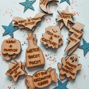 May include: A set of 12 wooden Halloween activity ideas, each with a different activity written on it. The activities include "Make a spooky dessert", "Carve a pumpkin", "Watch Hocus Pocus", "Get fun Halloween candy", "Pick out a costume", "Decorate the house", "Spooky movie marathon", "Find orange and black in nature", "Make caramel apples", "Halloween crafts".