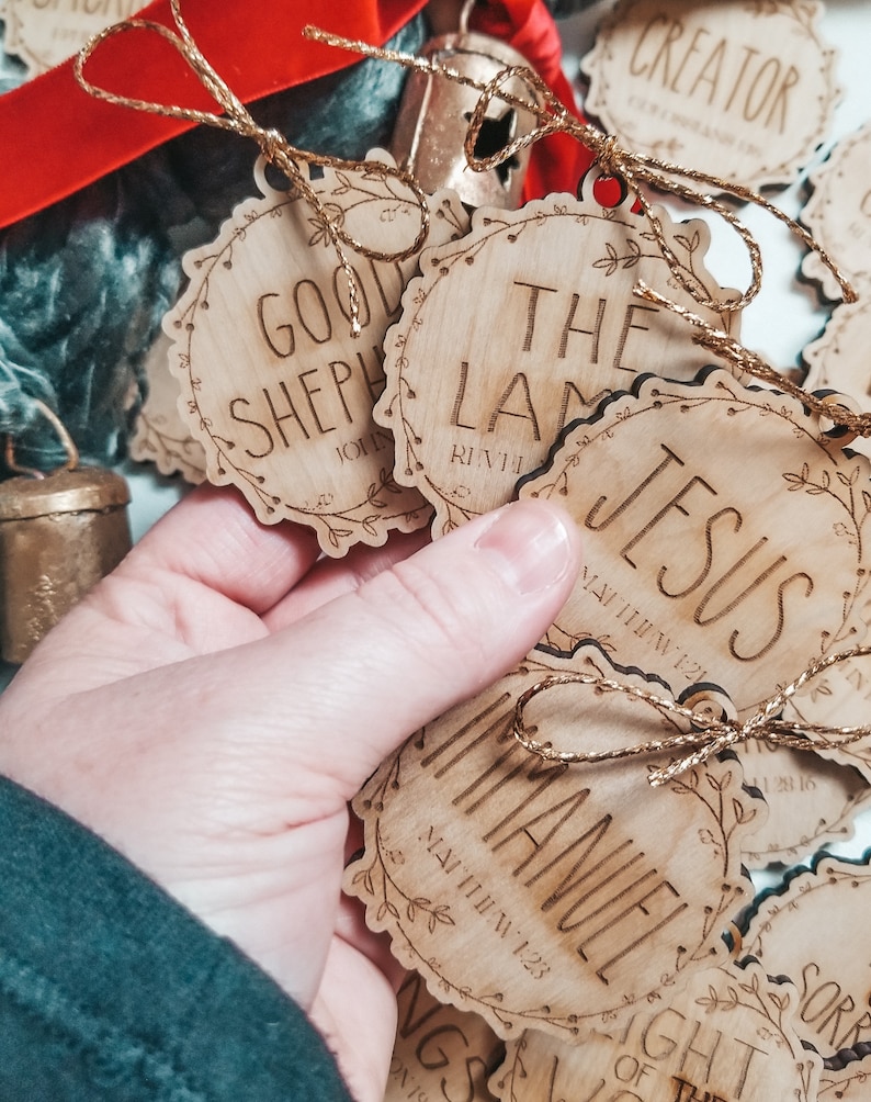 May include: Wooden Christmas ornaments with a rustic brown finish and gold string. Each ornament features a different Bible verse and phrase, including "Good Shepherd", "The Lamb", "Jesus", "Immanuel", and "Creator".