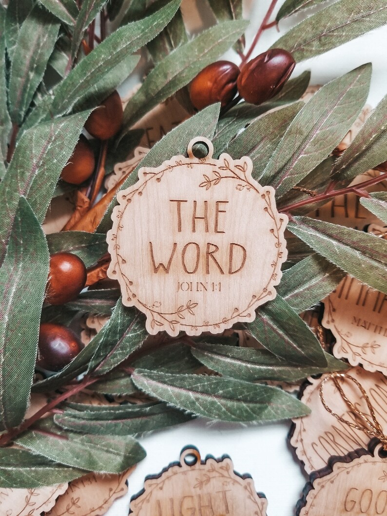 May include: Wooden ornament with a floral wreath design and the words "The Word" and "John 1:1" engraved on it.