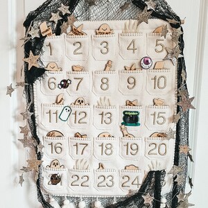 Peut inclure: Un calendrier de l'avent en feutre blanc avec 24 poches, chacune avec une image diff&eacute;rente sur le th&egrave;me d'Halloween. Le calendrier est d&eacute;cor&eacute; d'&eacute;toiles dor&eacute;es scintillantes et d'un tissu en maille noire.