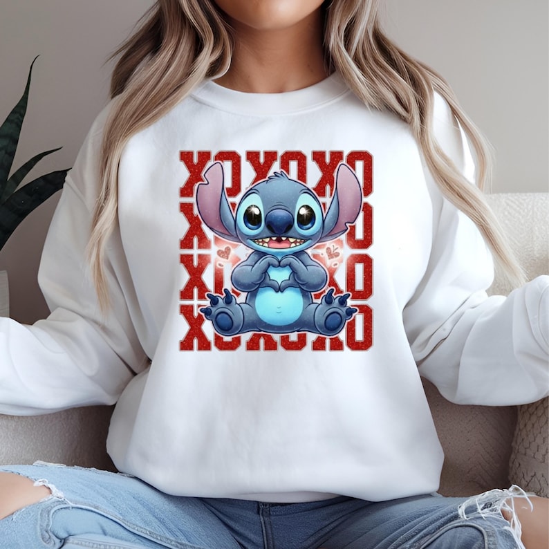 May include: White sweatshirt featuring a blue cartoon character with large ears, holding a heart shape with its hands. The design includes red "XOXO" text. The sweatshirt is a casual style.