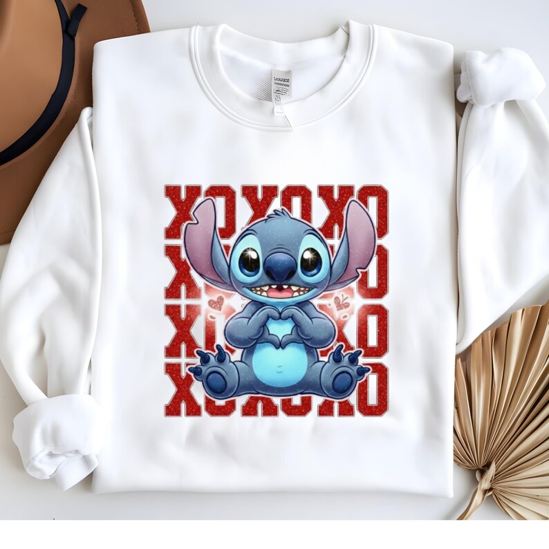 May include: White sweatshirt featuring a cartoon image of Stitch, a blue alien character, forming a heart with his hands. The design includes the text "XOXO" in red, with hearts. A casual, comfortable garment.