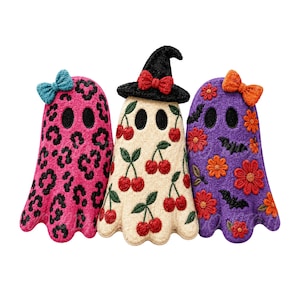 May include: Three ghost-shaped embroidered patches. The left is pink with a black leopard print and a teal bow. The centre is cream with red cherries and a black witch hat with a red bow. The right is purple with orange flowers and black bats.