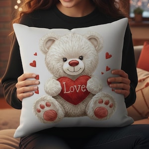 May include: White decorative pillow featuring a teddy bear holding a red heart with the word "Love". The bear has a red nose and paw pads, with small red hearts scattered around. A cozy, romantic theme.