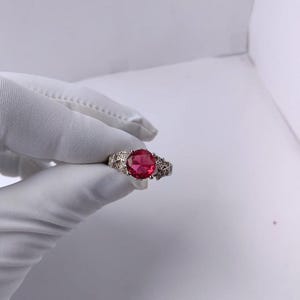 May include: A silver ring with a large, round, red gemstone. The ring has a decorative band with star-like cutouts. The gemstone is the focal point, set in a classic prong setting.