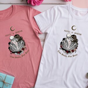 May include: Two t-shirts, one pink and one white, each featuring a graphic of two skeletons embracing, surrounded by roses. The text "ALEXI & SARAH" and "Two Souls, One Bone" are printed above and below the graphic, respectively.