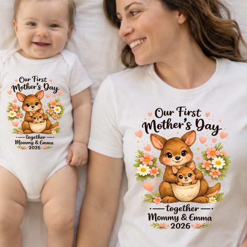 Może przedstawiać: Biała koszulka i body dla dziecka z grafiką kangura. Projekt zawiera tekst "Our First Mother's Day" i "together - Mommy & Emma 2026". Kangur jest brązowy z małym kangurem w torbie, otoczony kwiatami.
