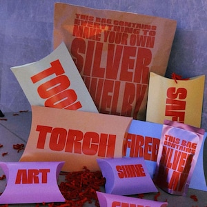 Può includere: Un assortimento di pacchi e sacchetti colorati con testo relativo alla creazione di gioielli. I pacchi sono di varie forme e colori, tra cui rosa, giallo e blu. Il testo include "TOOLS", "TORCH FIRED", "GEMS" e "SILVER".