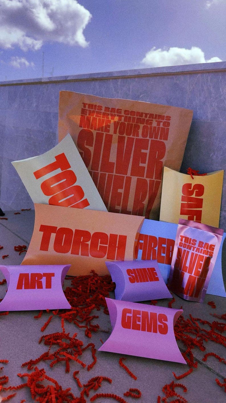 Pu&ograve; includere: Una collezione di scatole a cuscino e bustine di carta colorate con testo rosso. Gli articoli presentano etichette come "THIS BAG CONTAINS EVERYTHING TO MAKE YOUR OWN SILVER JEWELRY", "TOOLS", "TORCH FIRED", "ART", "SHINE", "GEMS" e "SILVER CLAY".