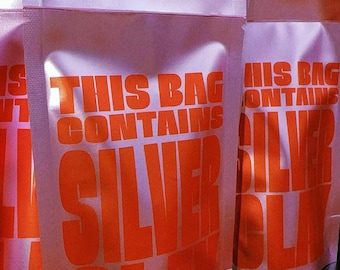 Peut inclure: Trois sachets debout rose clair avec un texte orange vif indiquant THIS BAG CONTAINS SILVER CLAY. Les sachets ont une finition mate et un bord supérieur thermoscellé, disposés verticalement en rangée avec le texte clairement visible.