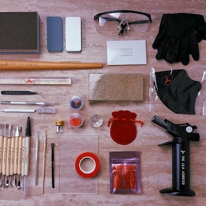 Pu&ograve; includere: Un kit per la lavorazione dell'argilla metallica che include un cannello a butano nero, occhiali protettivi, guanti neri, un mandrino in legno per anelli, vari strumenti di scultura, blocchi abrasivi, un sacchetto di velluto rosso, nastro rosso e argilla d'argento.