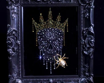 May include: A black ornate frame containing a dark background with a skull design formed by white crystals. The skull wears a gold crystal crown and features a gold crystal spider on the side, with dangling crystal strands hanging from the jaw.