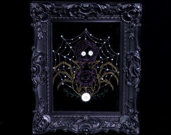 May include: A black ornate frame containing a dark fabric panel with an embroidered design of a figure with button eyes and a spider-like body. The artwork features a white spiderweb background, yellow spider legs, and three white buttons.