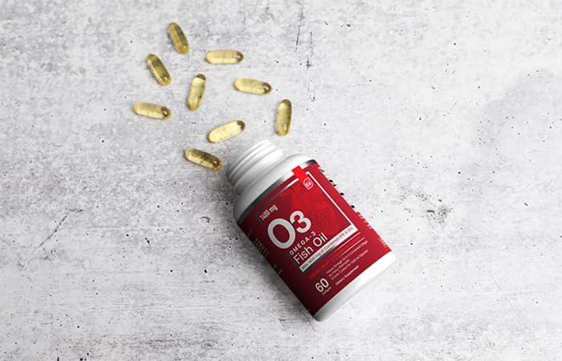 K&ouml;nnte beinhalten: Eine wei&szlig;e Flasche mit einem roten Etikett, das Omega-3-Fisch&ouml;l-Kapseln enth&auml;lt. Das Etikett zeigt den Text "O3 Fish Oil" und "1400 mg". Mehrere gelbe Kapseln sind um die Flasche herum auf einer grauen Oberfl&auml;che verstreut. Die Flasche enth&auml;lt 60 Kapseln.