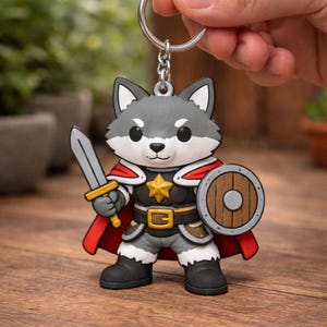 May include: A keychain featuring a cartoon wolf warrior with a sword and shield. The wolf is gray with a red cape, gold star, and black boots. The keychain is held by a silver ring.