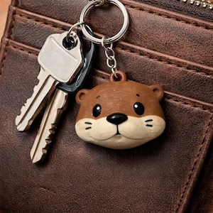 May include: A brown leather wallet with a zipper closure and a keychain with a cute otter-shaped charm. Two keys are attached to the keychain. The otter charm is brown and cream-colored with black eyes and a black nose.