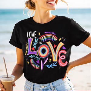 Könnte beinhalten: Schwarzes T-Shirt mit dem Schriftzug "Love is Love" in einem farbenfrohen, Regenbogen-Themen-Design. Das Design beinhaltet einen Regenbogen, Herzen und florale Elemente. Das Shirt hat einen Rundhalsausschnitt.