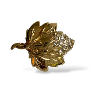 May include: A gold-toned leaf-shaped brooch with intricate detailing. The brooch features a cluster of sparkling clear crystals at the end, adding a touch of glamour. The design is reminiscent of nature, suitable for adding a decorative accent.