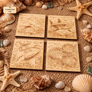May include: Four square wooden coasters with engraved ocean-themed designs. Each coaster features a different marine life illustration: a killer whale, a shark, a whale, and sea urchins. The coasters are made of light-colored wood.