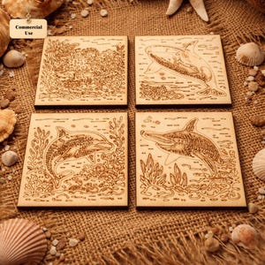 May include: Four square wooden coasters with engraved marine life designs. One coaster features coral, another an orca, and two depict dolphins. The coasters are light brown and set on a burlap surface with seashells.