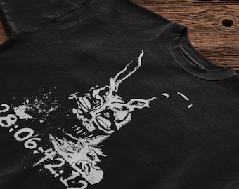 May include: A black t-shirt featuring a white graphic print of a rabbit-like creature with long ears and the text 28:06:42:12 printed in a distressed, stencil-style font. The design is positioned on the front of the garment with a crew neckline.