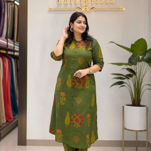 May include: An olive green kurta and matching pants set with a floral print in red and yellow. The kurta has a button-down front and three-quarter sleeves. The image also shows the text "Lavish Enterprises" in gold lettering.