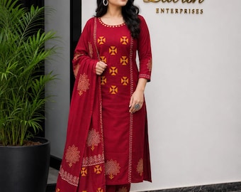 May include: A burgundy three-piece suit featuring a long-sleeve tunic, matching pants, and a shawl. The tunic and pants are adorned with a repeating yellow cross pattern. The shawl has a floral and geometric design. The suit is worn with gold-colored flats.