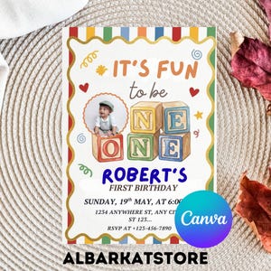Puede incluir: Una colorida invitación de primer cumpleaños con el texto "It's Fun to be ONE" y "Robert's First Birthday". El diseño incluye una foto de bebé, bloques de juguete y elementos decorativos. La invitación es de ALBARKATSTORE.