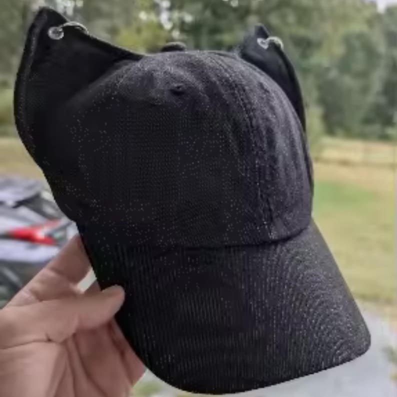 Puede incluir: Gorra de b&eacute;isbol negra con detalles en forma de orejas y anillos de metal plateado. La gorra tiene una visera curva y una tela texturizada con sutiles detalles brillantes. Un dise&ntilde;o &uacute;nico.