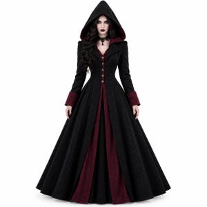 Può includere: Un cappotto lungo fino ai piedi con cappuccio, caratterizzato da un esterno nero e una fodera interna color bordeaux intenso. Il cappotto presenta maniche lunghe con polsini bordeaux, chiusura frontale con bottoni e un corpetto strutturato.