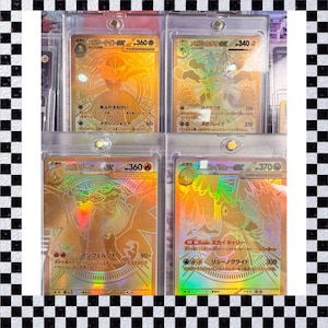 Puede incluir: Cuatro cartas coleccionables doradas en fundas protectoras. Cada carta presenta un diseño holográfico con texto japonés e ilustraciones de personajes. Cartas de un juego de cartas coleccionables.