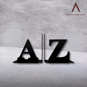 Puede incluir: Soportes para libros de metal negro con forma de las letras A y Z. Se muestran sobre una superficie gris. El texto "ATLANTIS STEEL CRAFT" está en la esquina superior derecha.