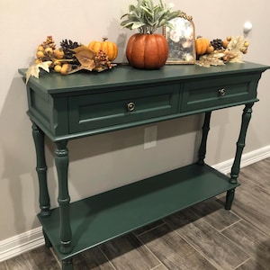 May include: A white ceramic mug with a black handle and the text "But First, Coffee" in a black, bold font. The mug is sitting on a wooden surface. The mug is empty.