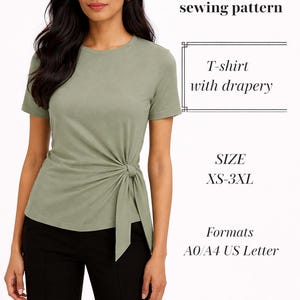 May include: A woman wearing a sage green t-shirt with a draped knot detail. The image includes text that reads "PDF sewing pattern", "T-shirt with drapery", "SIZE XS-3XL", and "Formats A0/A4 US Letter". The model is also wearing black pants.