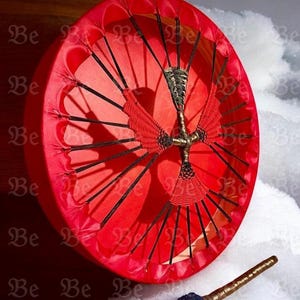 May include: A bright red drum with a central decorative design and black detailing. The drum is shown with a mallet, featuring a blue head and a gold-coloured handle. The background has a snowy texture.