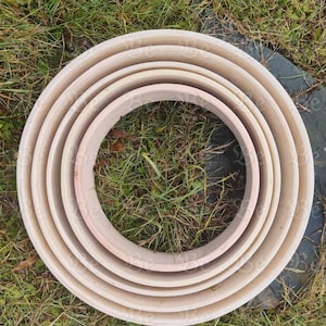 Puede incluir: Un conjunto de seis anillos de madera sin terminar de diferentes tamaños, anidados entre sí. Los anillos son de color beige claro y parecen estar hechos de madera contrachapada. Los anillos están dispuestos sobre hierba verde.