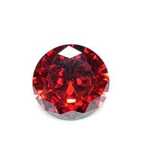 May include: A round, faceted gemstone with a deep, vibrant red color. The stone features a brilliant cut with numerous triangular and kite-shaped facets that reflect light, creating a complex pattern of bright red highlights and dark shadows.